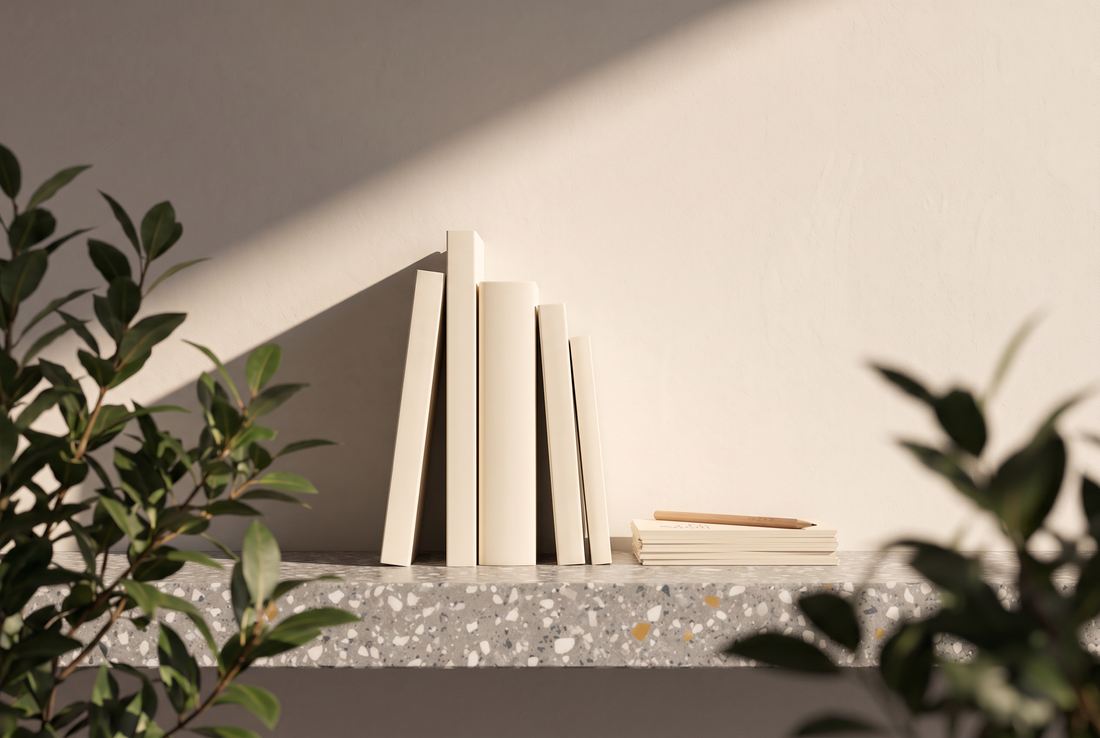 Aufrecht stehende Taschenbücher unterschiedlicher Größe mit leeren Buchrücken, ein Stapel Karteikarten und ein Bleistift auf einer Terrazzokante vor heller Wand in der Sonne