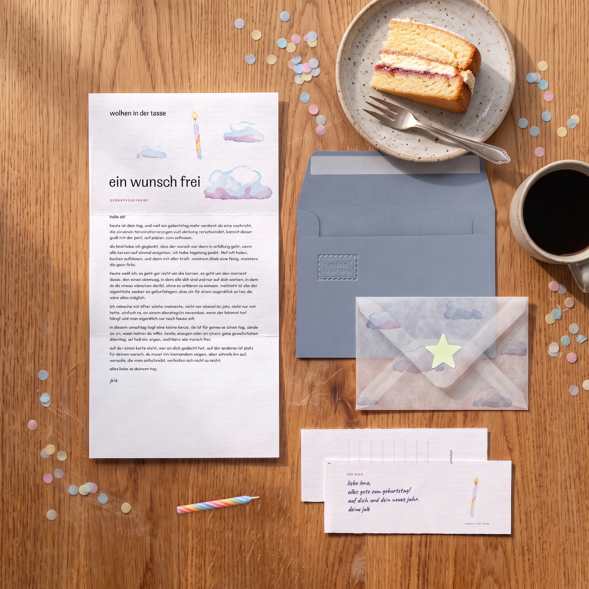 Geburtstagsbrief „ein wunsch frei“ auf einem Eichentisch mit Kuchenstück, Kaffee, Konfetti, Grußkarte und graublauem Umschlag